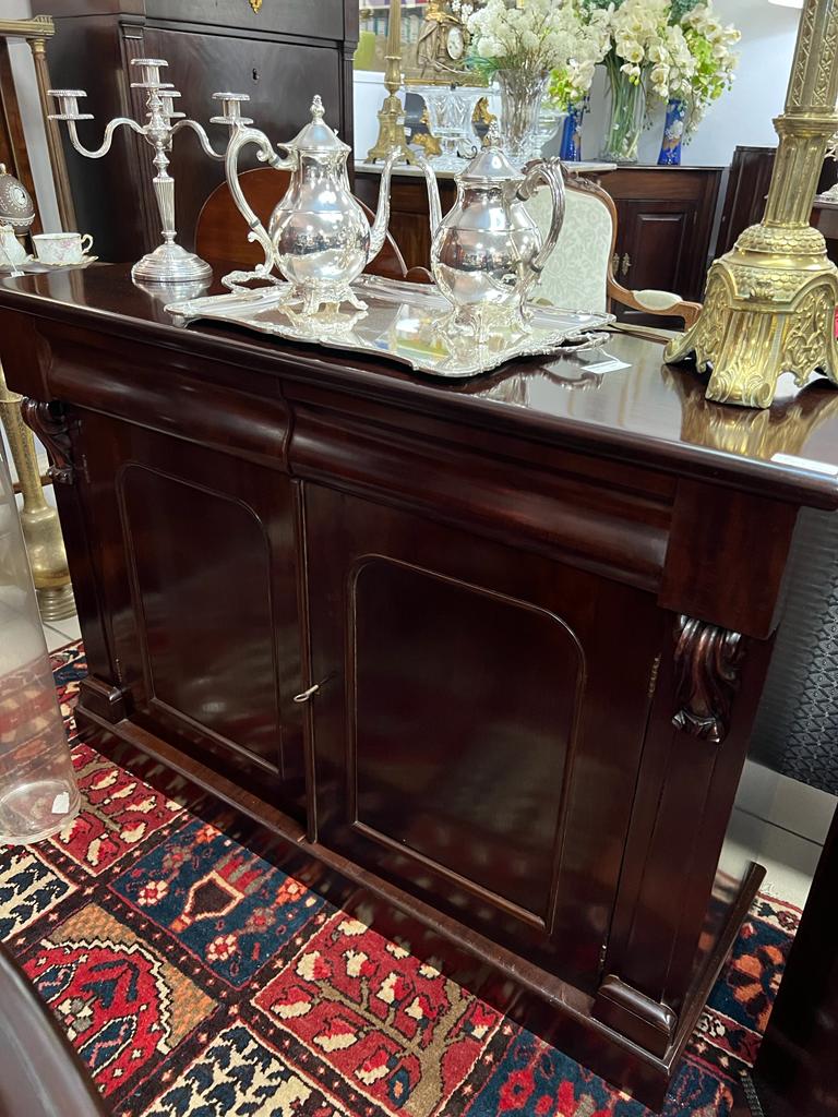 Meuble de couleur sombre avec de l'argenterie dessus et un tapis rouge en dessous