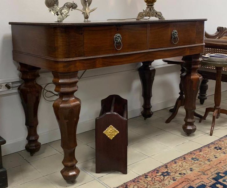 Bureau en bois foncé avec deux tiroirs et des pieds ornés, dans une pièce avec un tapis et une table d'appoint.