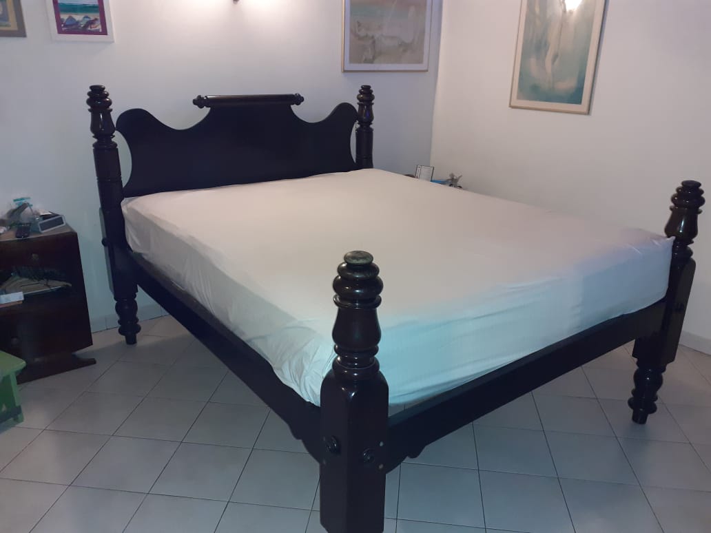 Lit à colonnes simple avec drap blanc, sur carrelage blanc et devant un mur blanc