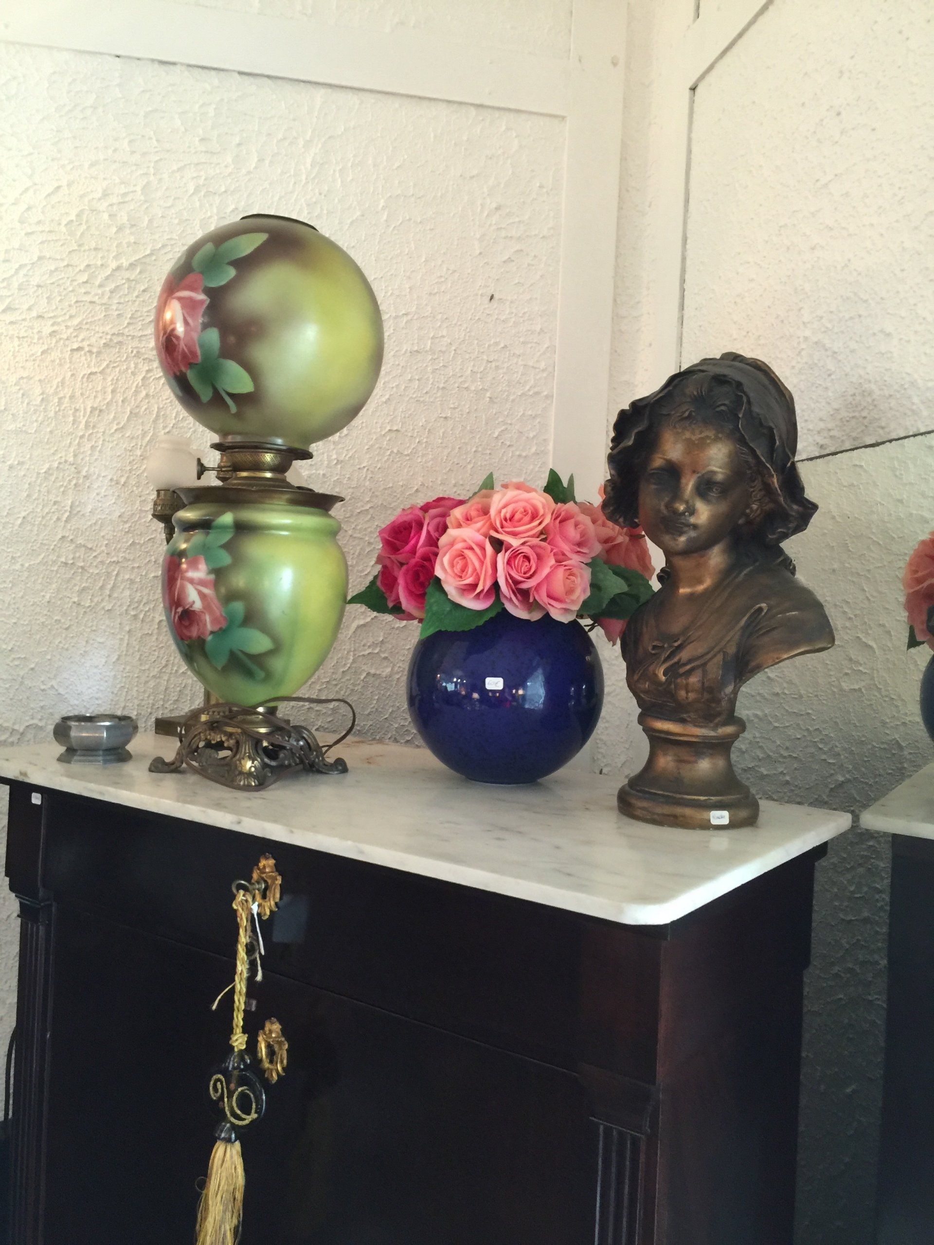 Table avec un vase de roses, un buste et une lampe verte