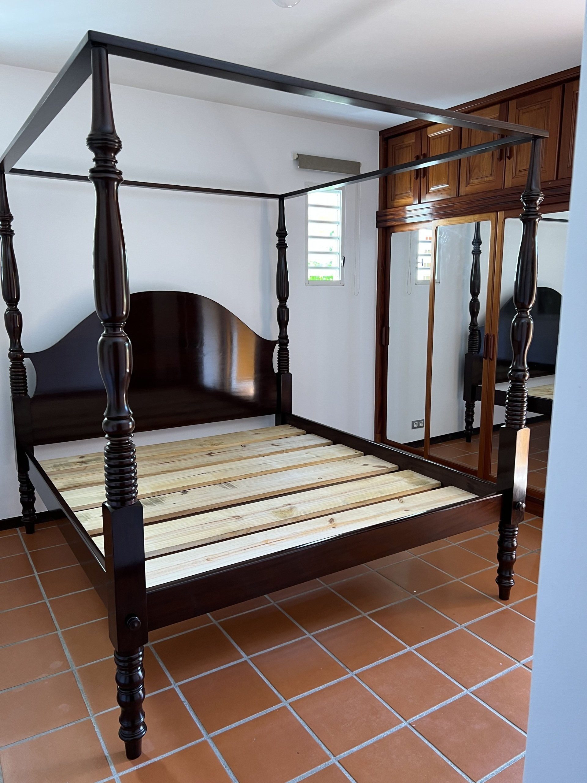 Cadre de lit à baldaquin en bois foncé dans une chambre avec sol carrelé et armoire à miroir.