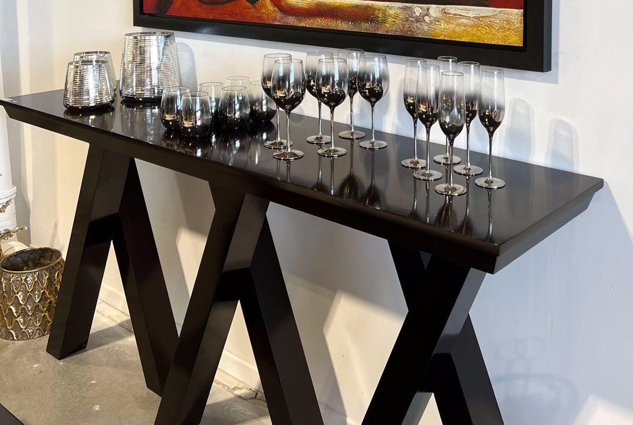 Console noire avec verres à pied et verres disposés sur le dessus, devant un mur blanc et des œuvres d'art.