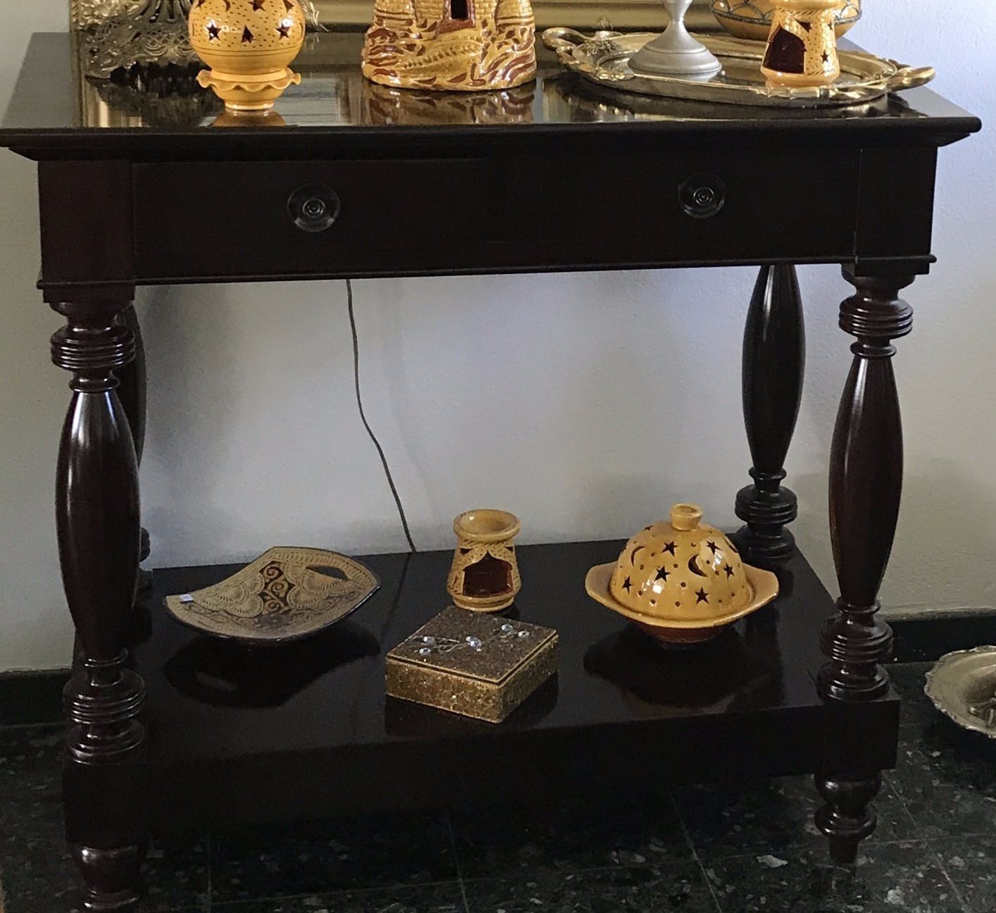 Table en bois foncé avec deux tiroirs, une étagère et des objets décoratifs.