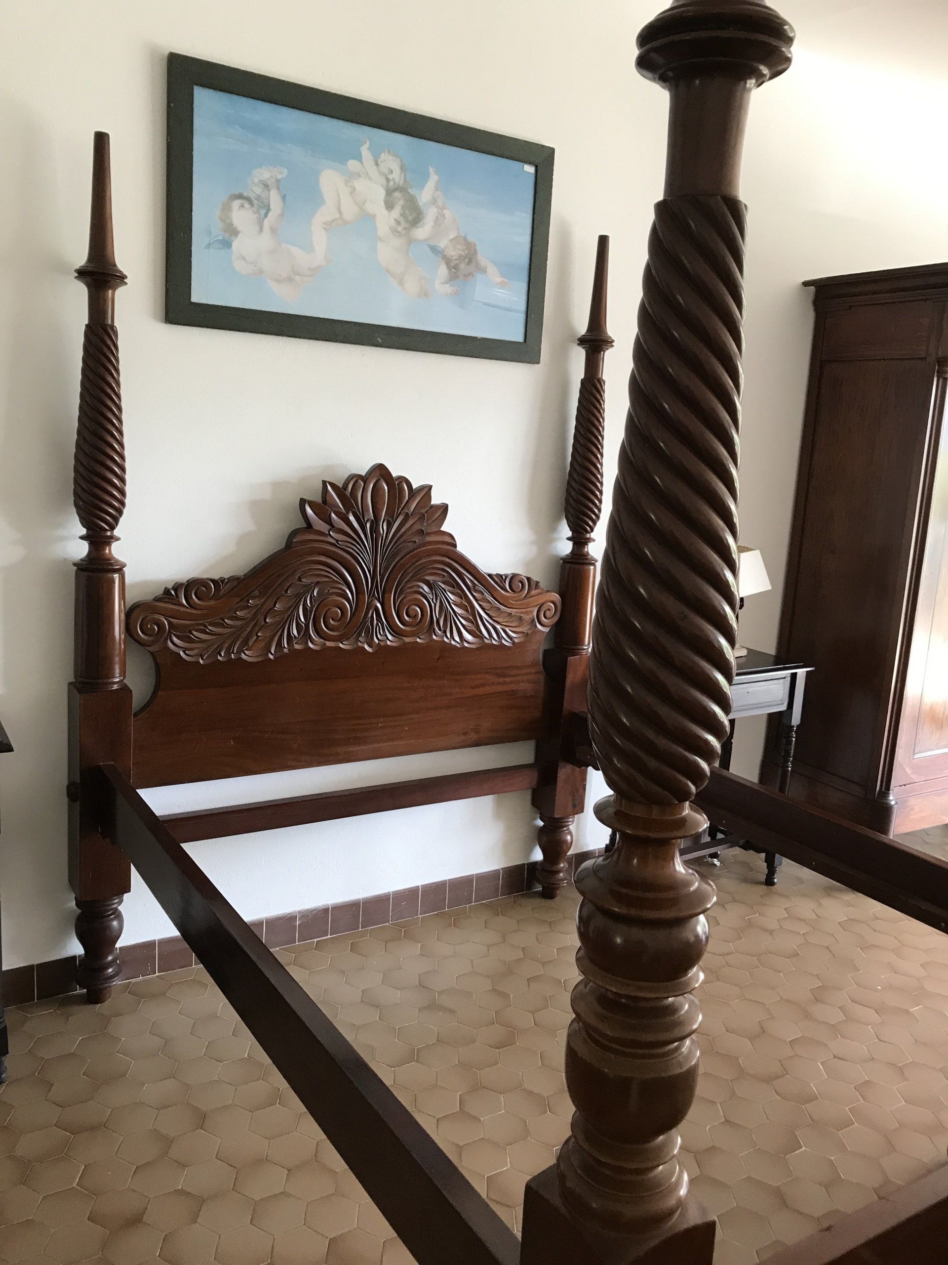 Structure de lit à baldaquin à côté d'une table de nuit avec sa lampe et d'une armoire