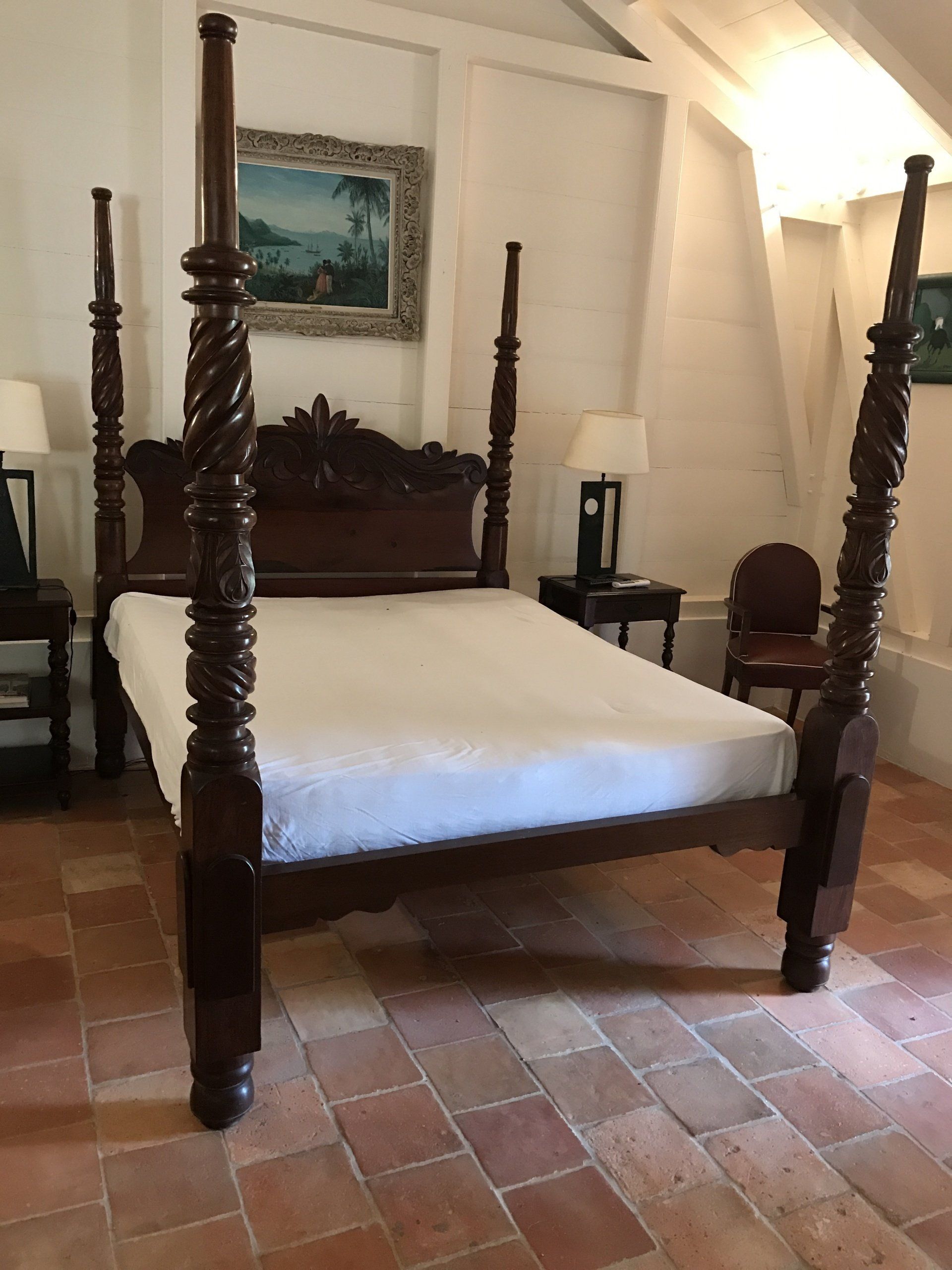 Lit à baldaquin sur carrelage avec drap blanc, entouré par deux petites tables de nuit