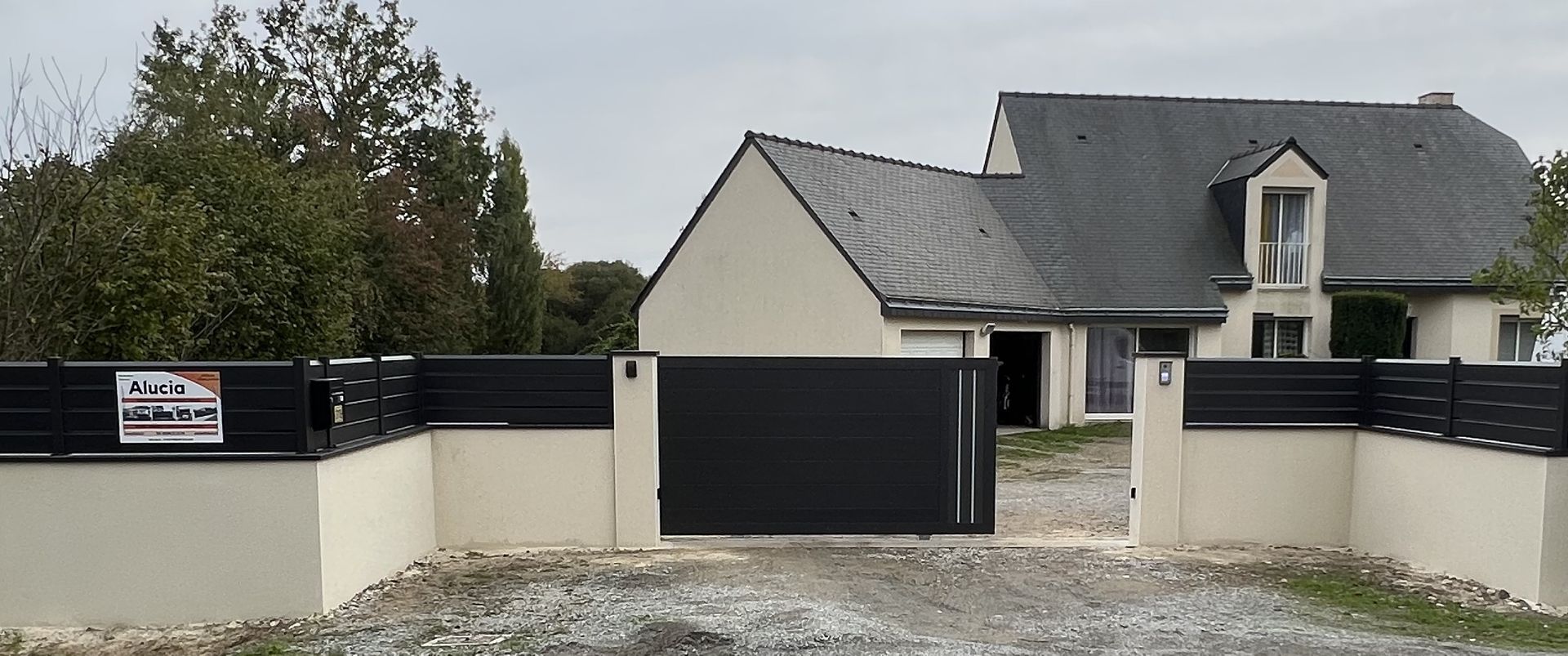 Portail coulissant en aluminium soudé motorisé avec sa clôture alignée en aluminium lames obliques posée sur un muret vue extérieure