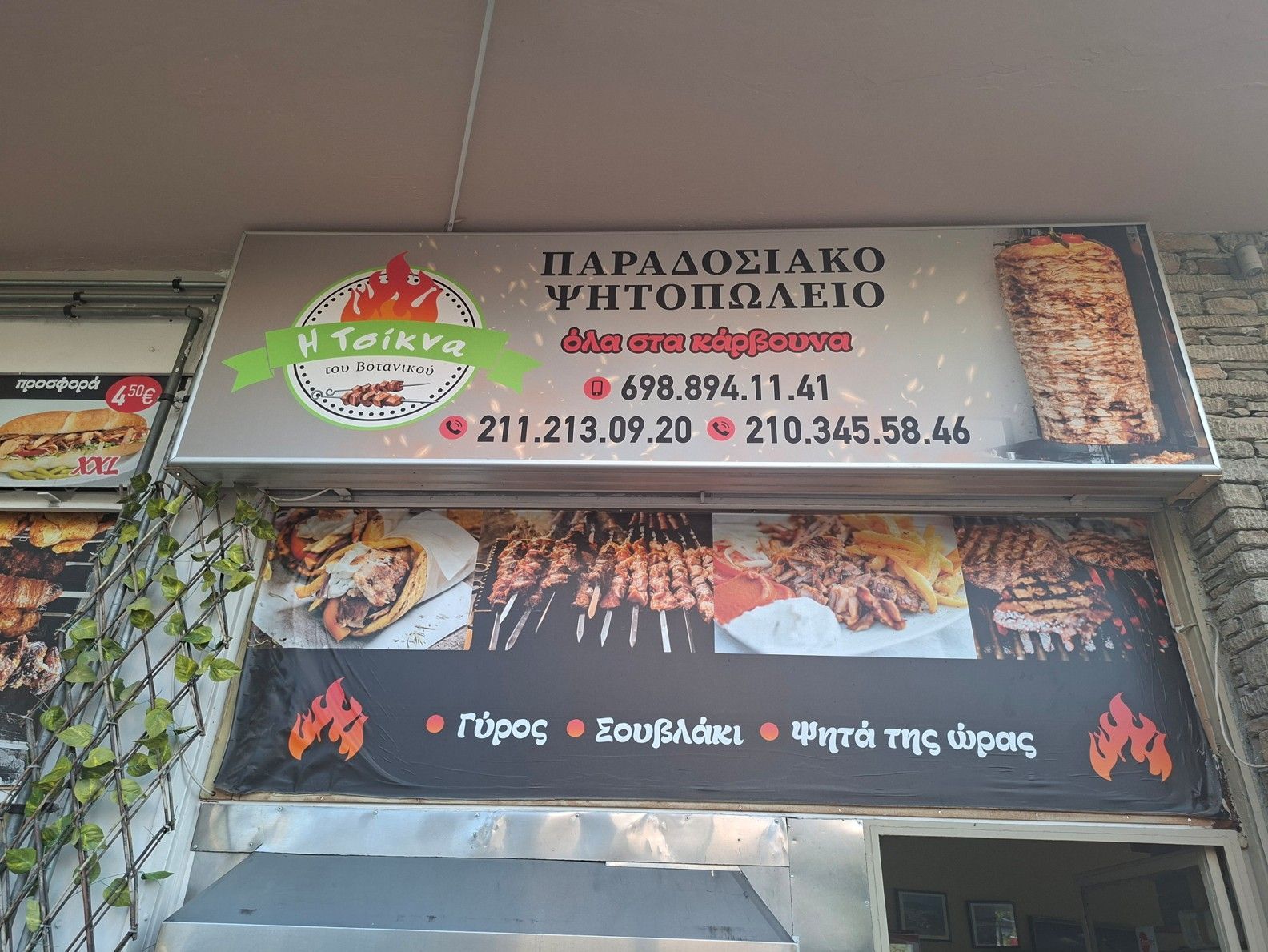 Πινακίδα βιτρίνας ελληνικού εστιατορίου με φωτογραφίες από το μενού και κρεμαστές κληματαριές πάνω από την είσοδο