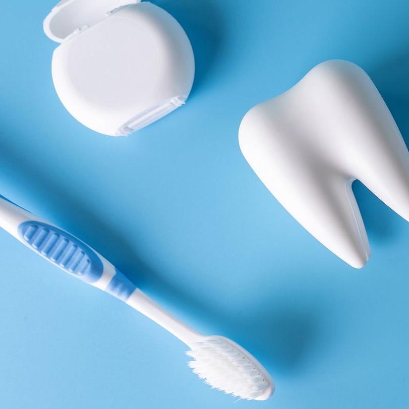 Brosse à dents, fil dentaire et dent sur fond bleu.
