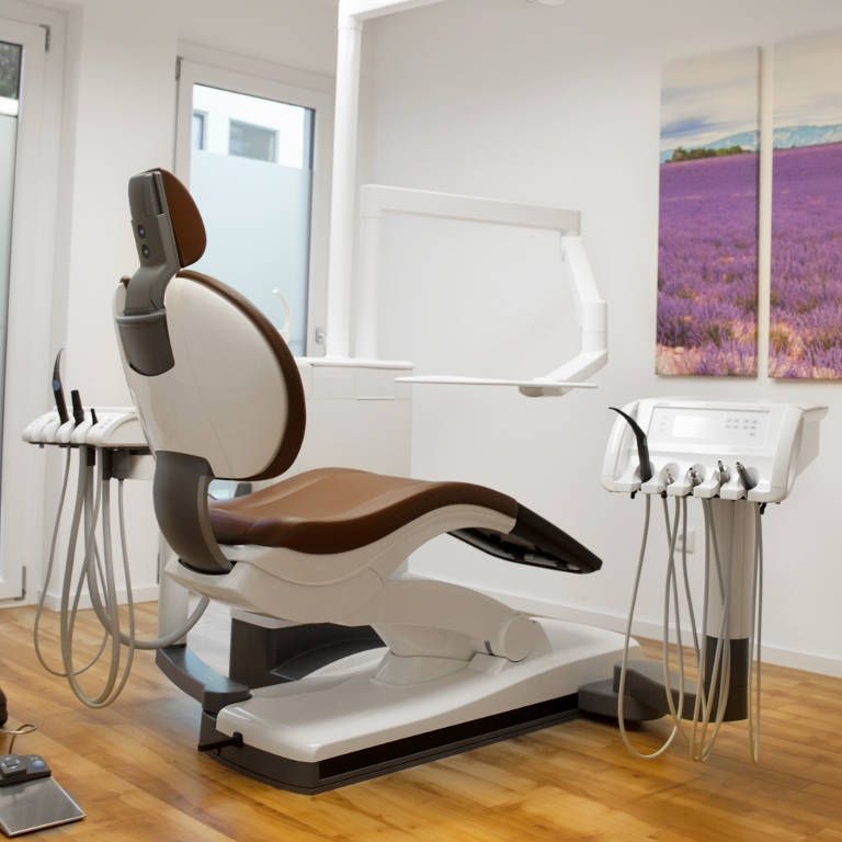 Moderner Behandlungsraum mit weißer Ausstattung und lila Wandbild.