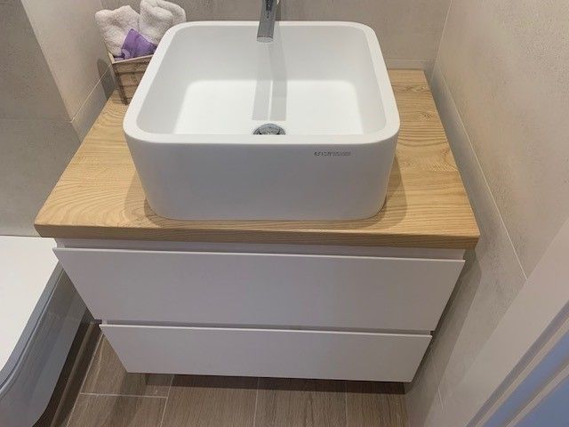 Un lavabo blanco está colocado encima de un mostrador de madera en un baño.