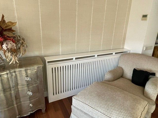 Una sala de estar con una silla, una otomana, una cómoda y una funda para radiador.