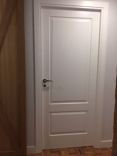 Una puerta blanca está en un pasillo al lado de una puerta de madera.