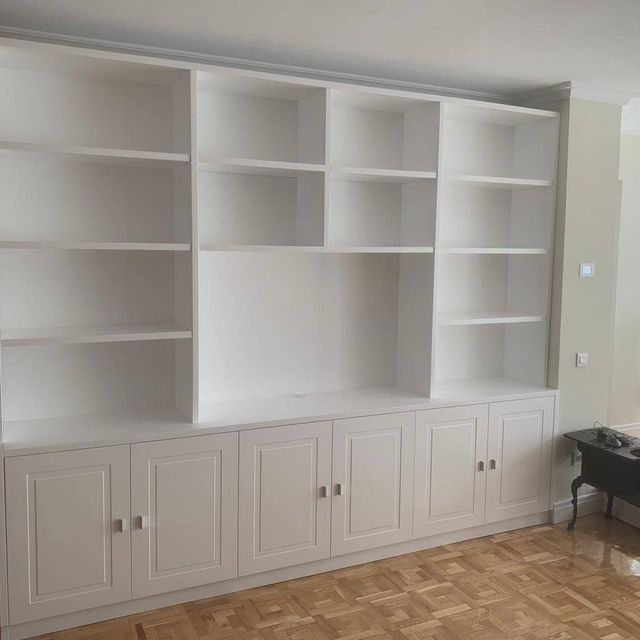 Una sala de estar con muchos estantes y armarios blancos.