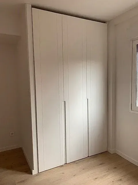Un dormitorio con un gran armario blanco y una ventana.
