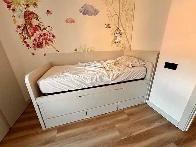 Una cama con cajones debajo en una habitación con una niña en la pared.