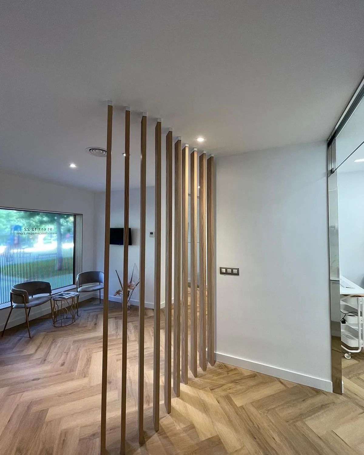 Una sala de espera con un separador de madera y suelo en espiga.