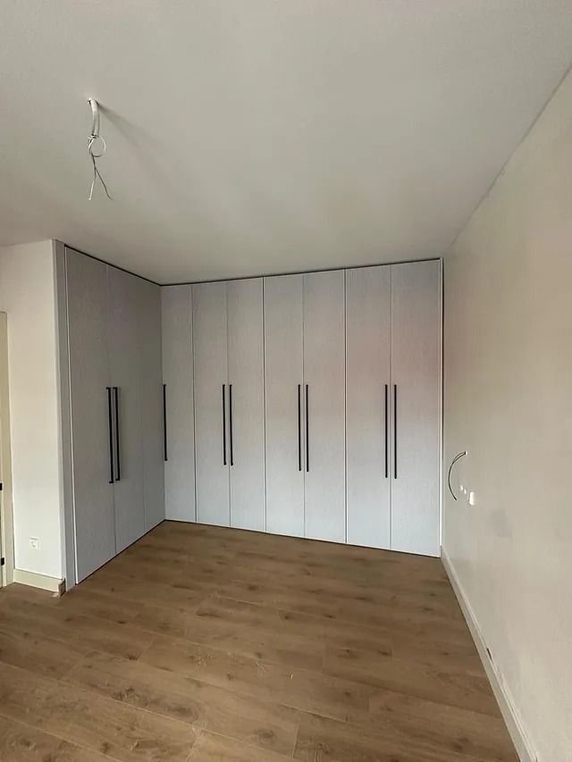 Una habitación con muchos armarios blancos y suelos de madera.