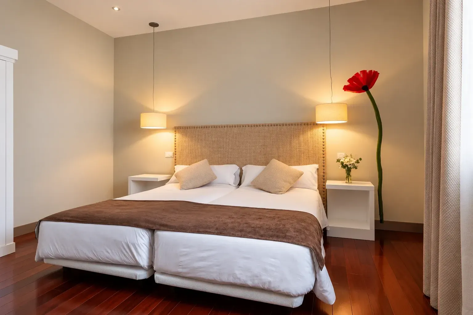 Habitación de hotel pequeña con dos camas blancas, pared gris, ventana y aire acondicionado.