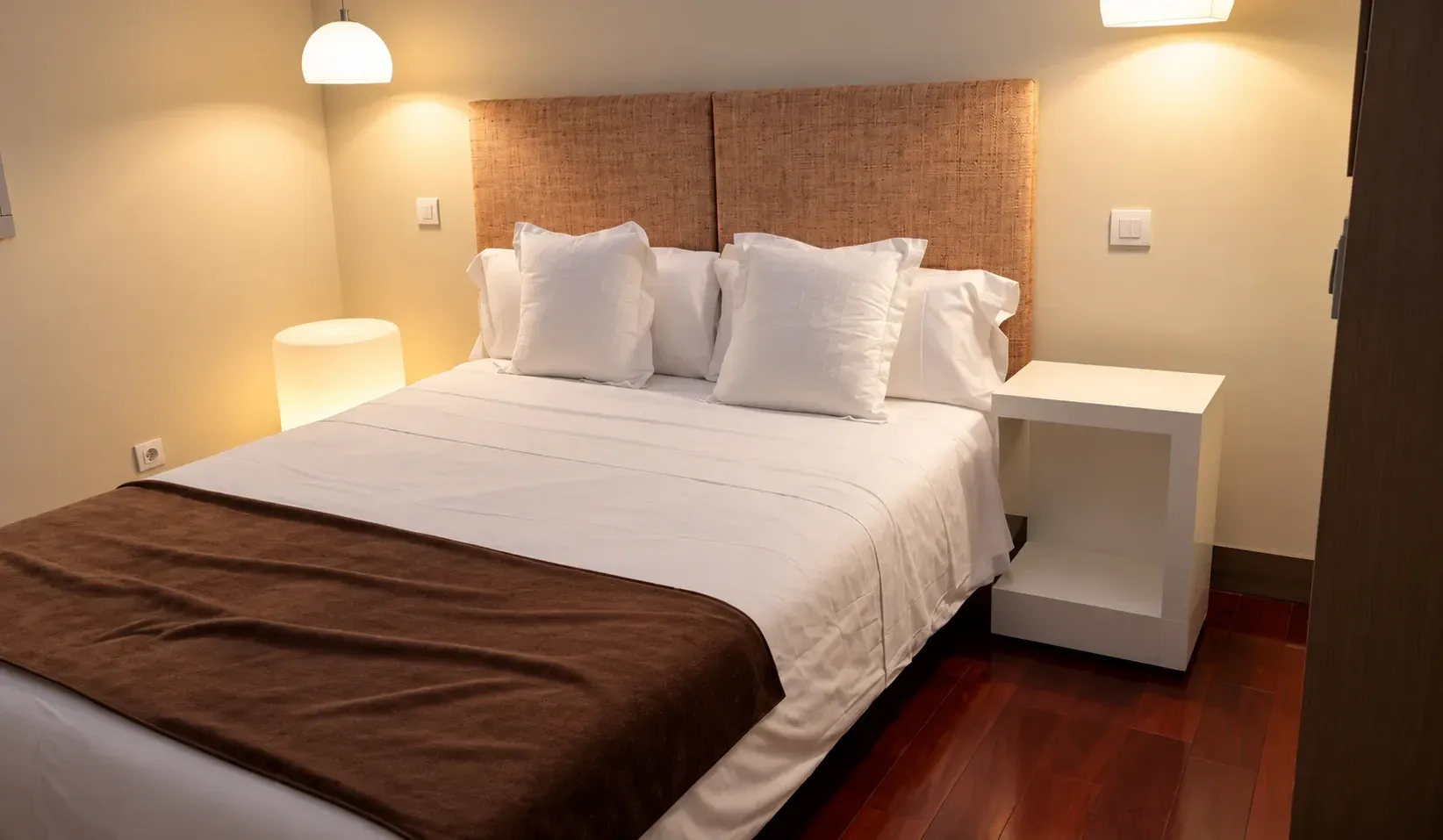 Acogedora habitación con cama blanca, cabecero de metal, cortinas rojas y una pequeña mesita de noche con flores.