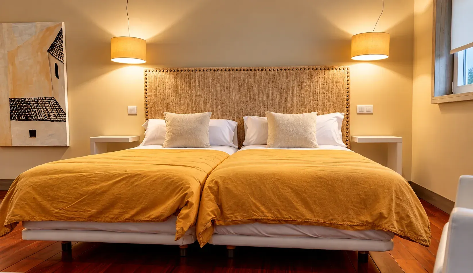 Acogedora habitación de hotel con dos camas individuales, colchas color mostaza y cálidas lámparas de mesilla