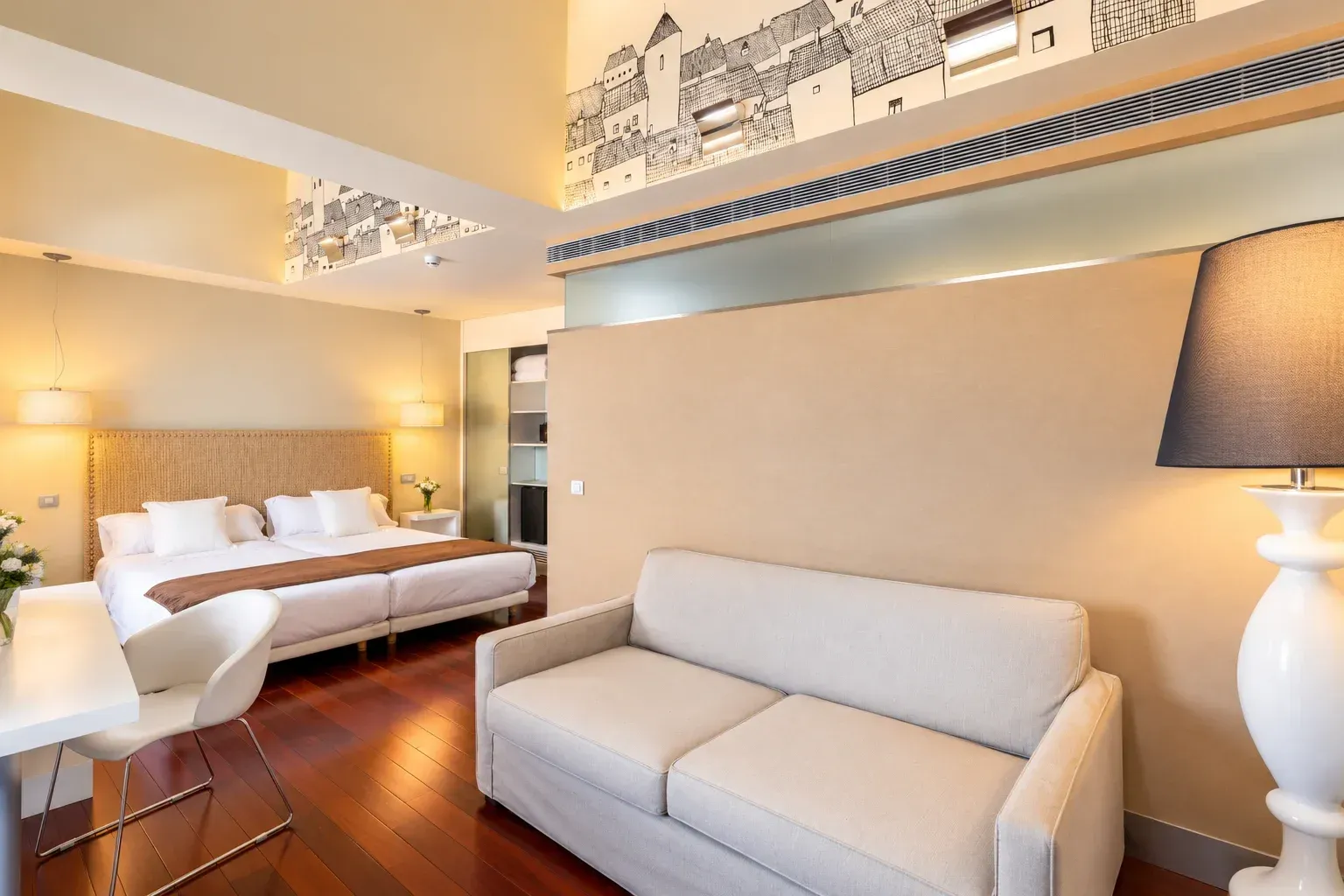 Habitación de hotel luminosa con sofá blanco, cama, suelo de madera y una cálida decoración en tonos beige