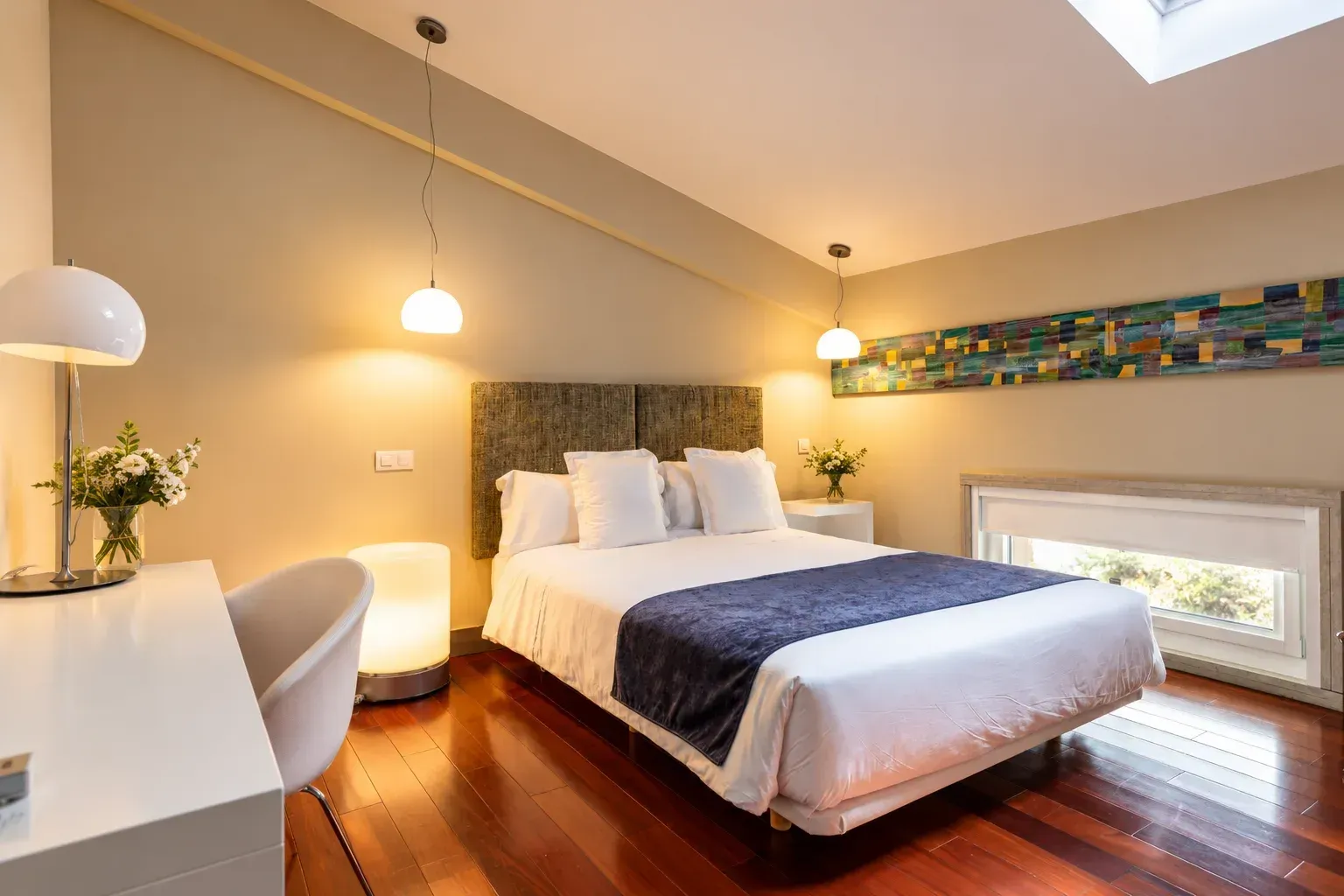 Dormitorio moderno con una cama, un escritorio, iluminación cálida y suelo de madera