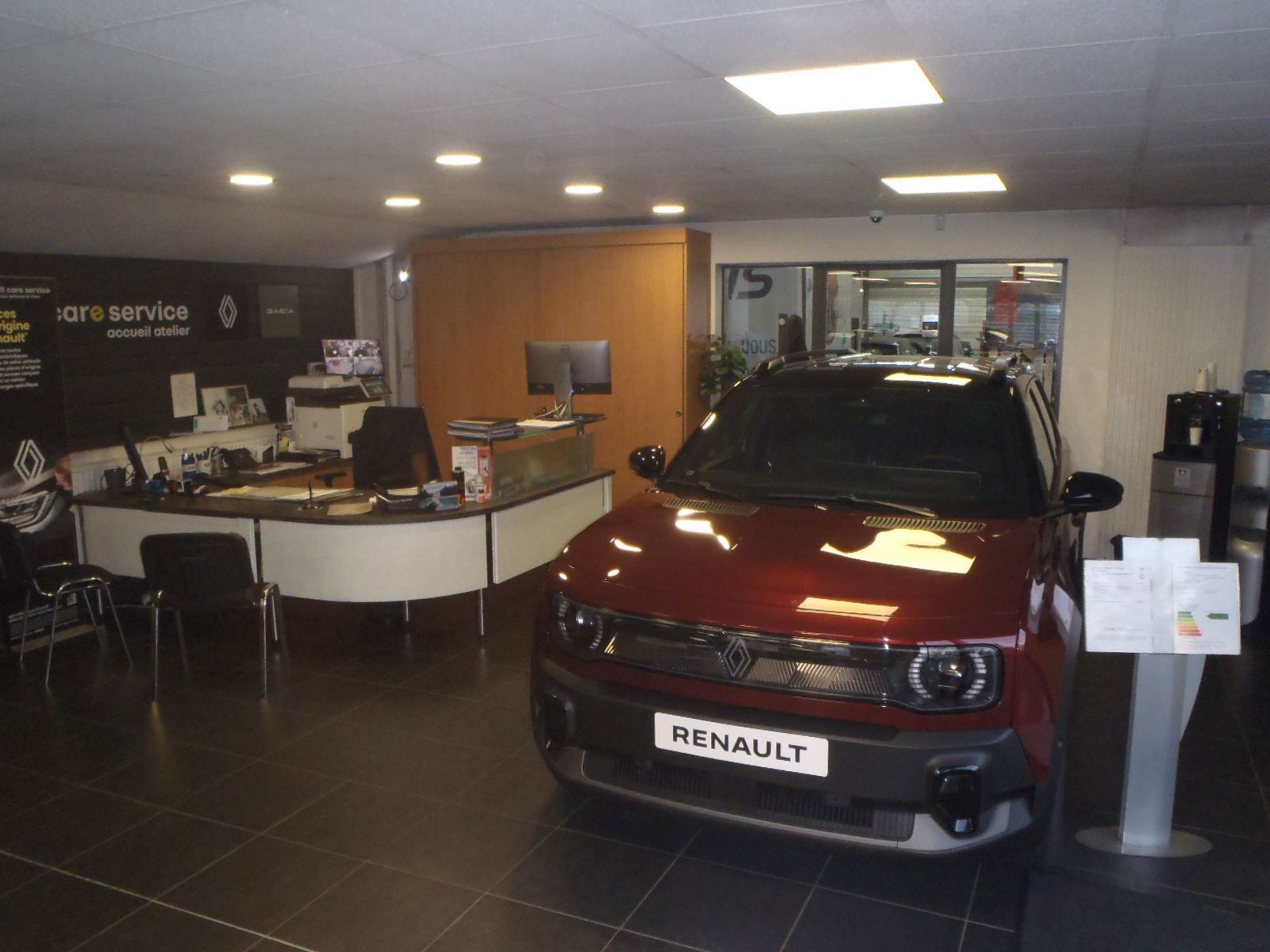 Intérieur d'une concession Renault. Une voiture rouge est exposée près d'un bureau.