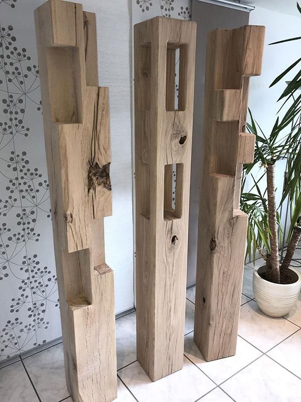 Drei Holzsäulen stehen auf einem gefliesten Boden neben einer Topfpflanze.
