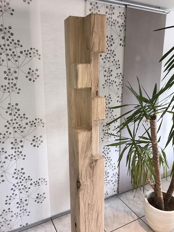 Eine Holzskulptur steht in einem Raum neben einer Topfpflanze.