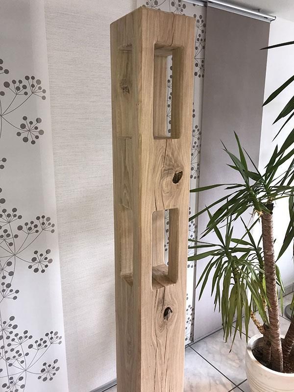 Eine Holzskulptur steht neben einer Topfpflanze in einem Raum.