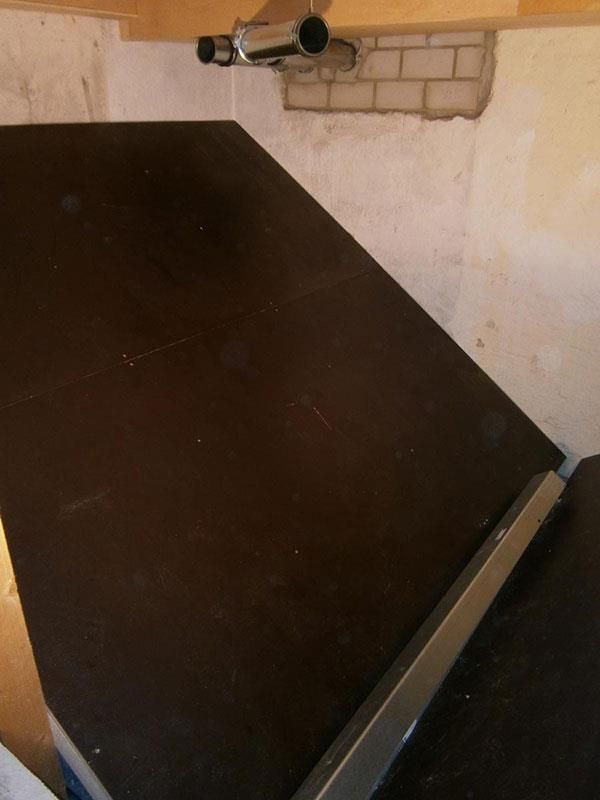 Ein schwarzer Tisch mit Metallgeländer steht in einem Raum neben einer Backsteinwand.