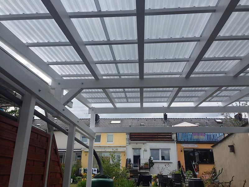 Eine weiße Pergola mit einem durchsichtigen Dach und einem Haus im Hintergrund