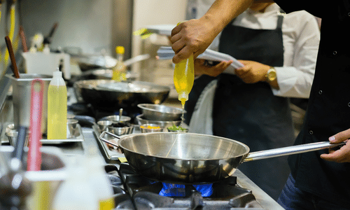 A man is pouring oil into a frying pan in a kitchen.
