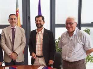 Tres hombres están de pie alrededor de una mesa con banderas en el fondo.