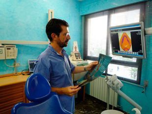 Un hombre está sentado en una silla dental mirando una radiografía.