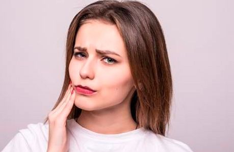 Una mujer se sostiene la cara con dolor a causa de un dolor de muelas.