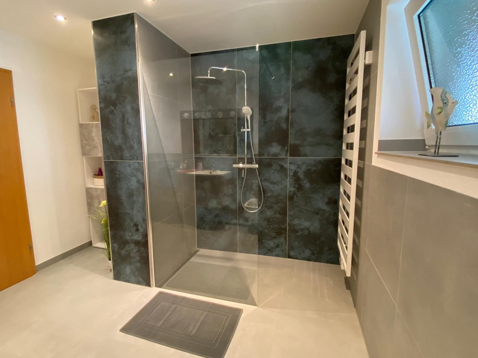 Modernes Badezimmer mit dunkelblau gefliester Dusche, Glastür und weißem Handtuchhalter.