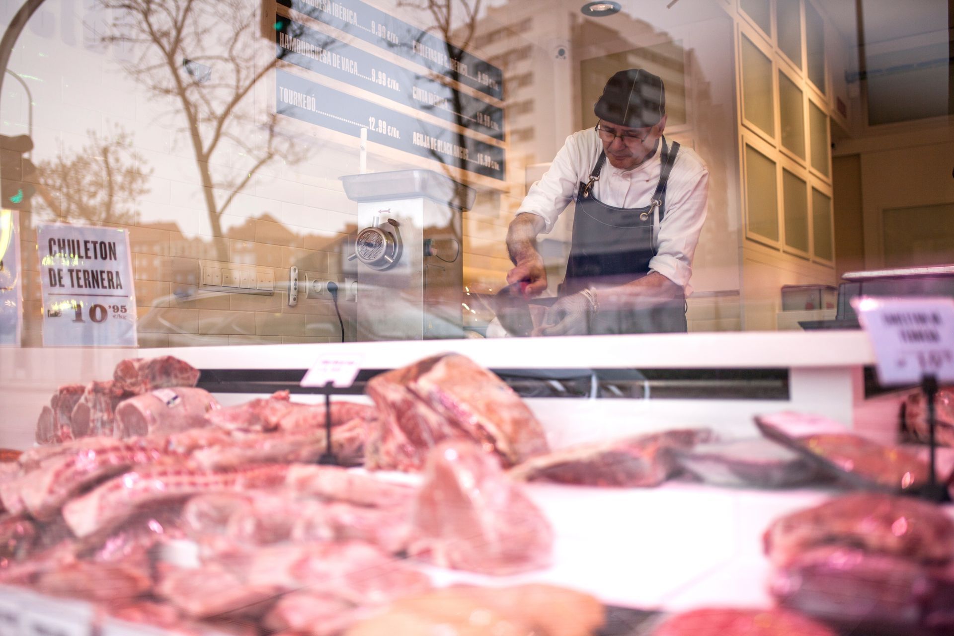 Boucher découpant de la viande en vitrine, différentes coupes exposées, en journée.