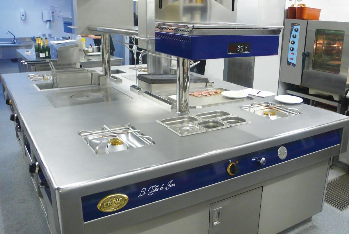 Îlot de cuisine professionnel avec plan de travail en acier inoxydable, brûleurs à gaz et poste de maintien au chaud des aliments.