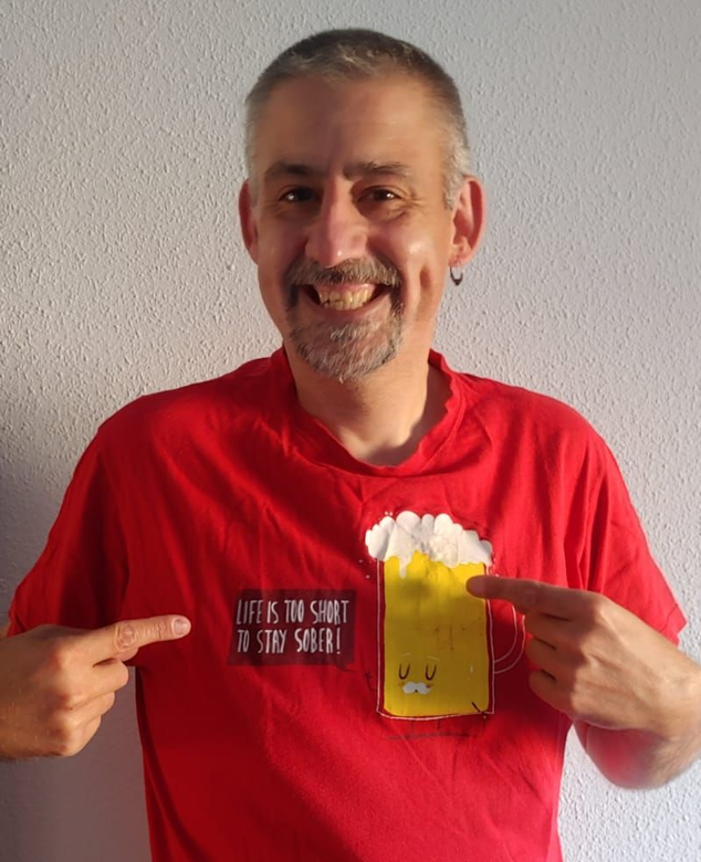 Persona sonriente con una camiseta roja señalando un gráfico y texto de cerveza en la camiseta.