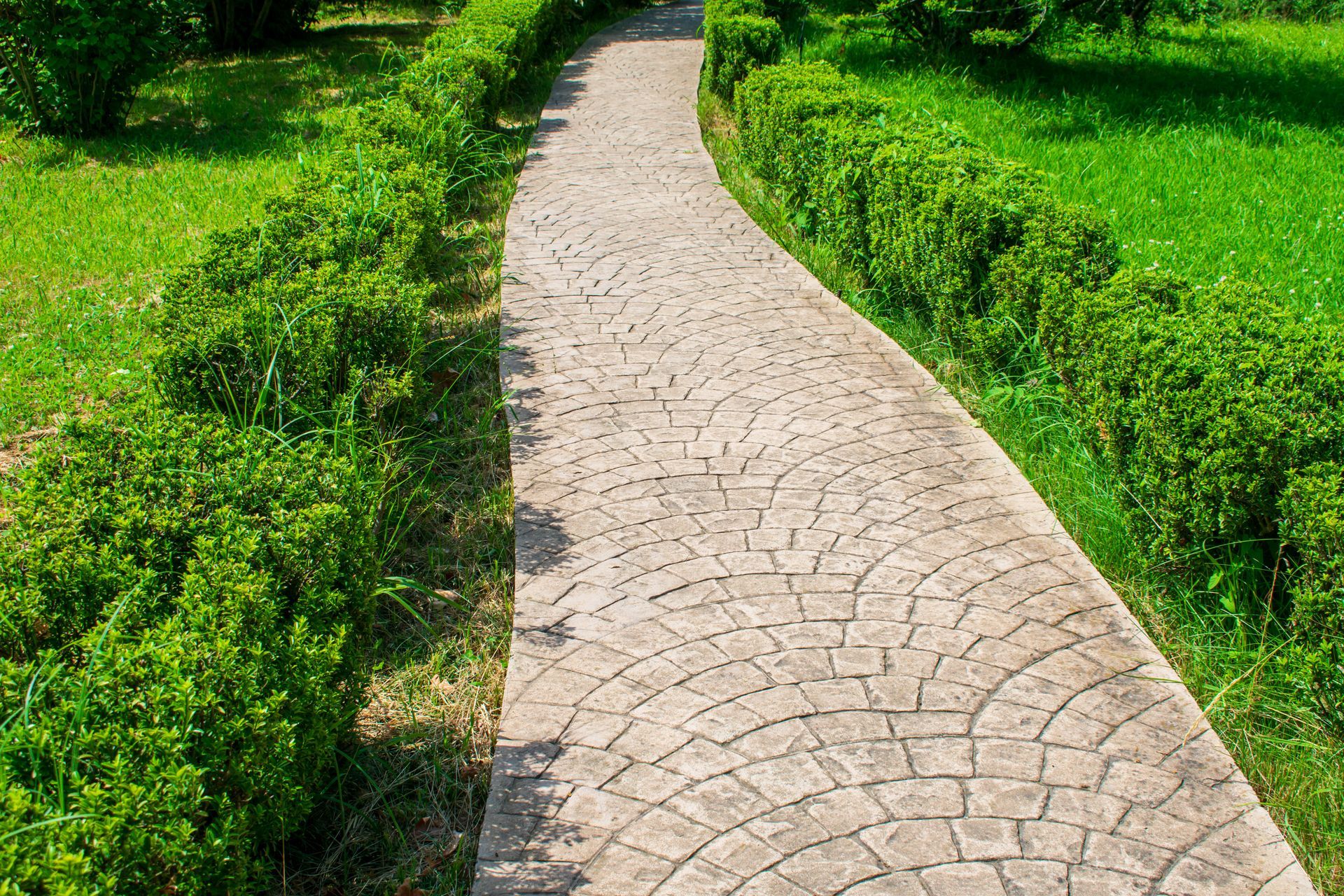 Chemin pavé sinueux traversant un parc verdoyant bordé de haies taillées et de pelouse.