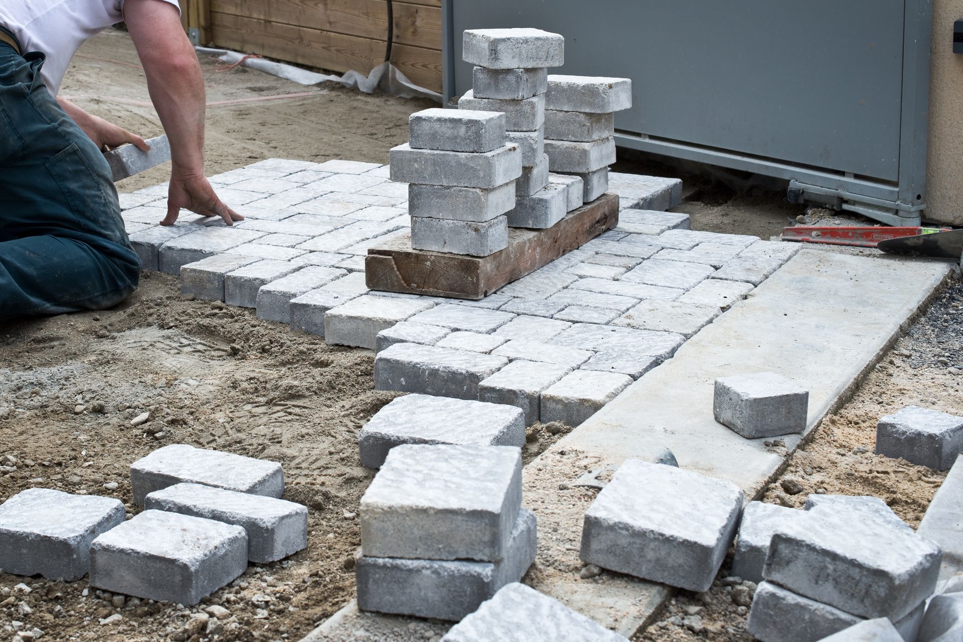 Ouvrier posant des pavés gris dans une terrasse en construction.