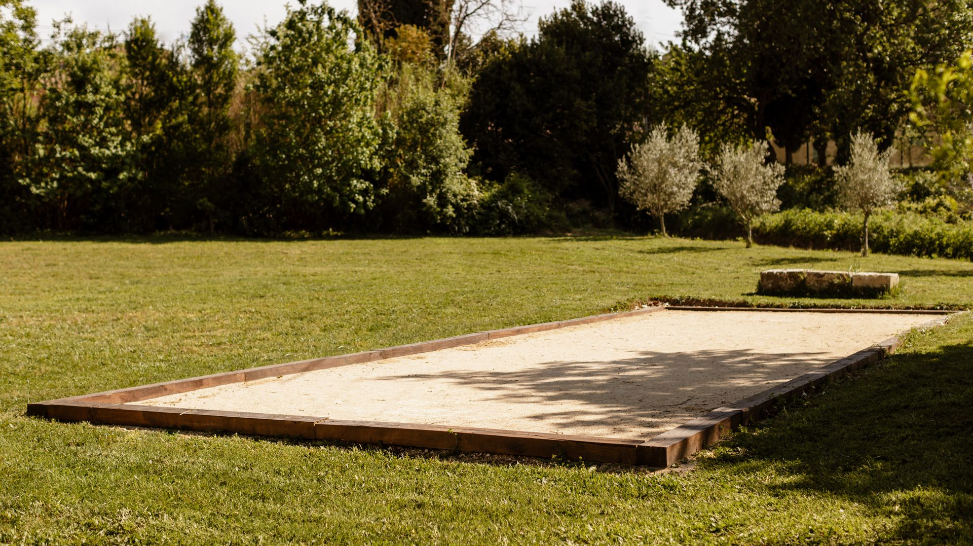 Terrain de pétanque entouré d'une pelouse, bordée d'arbres et d'arbustes.