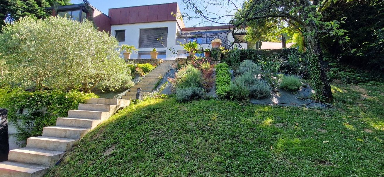 Des marches abruptes mènent à une maison située sur une colline verdoyante et ensoleillée.