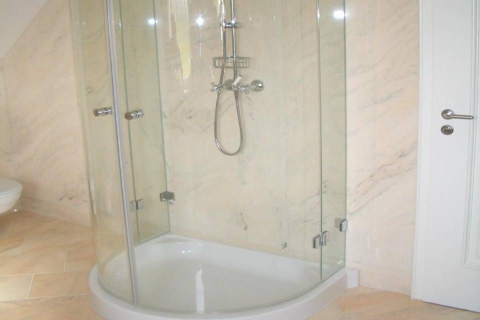 Duschkabine mit Glastüren, weißem Boden und Chromarmaturen in einem Badezimmer mit hellen Wänden.