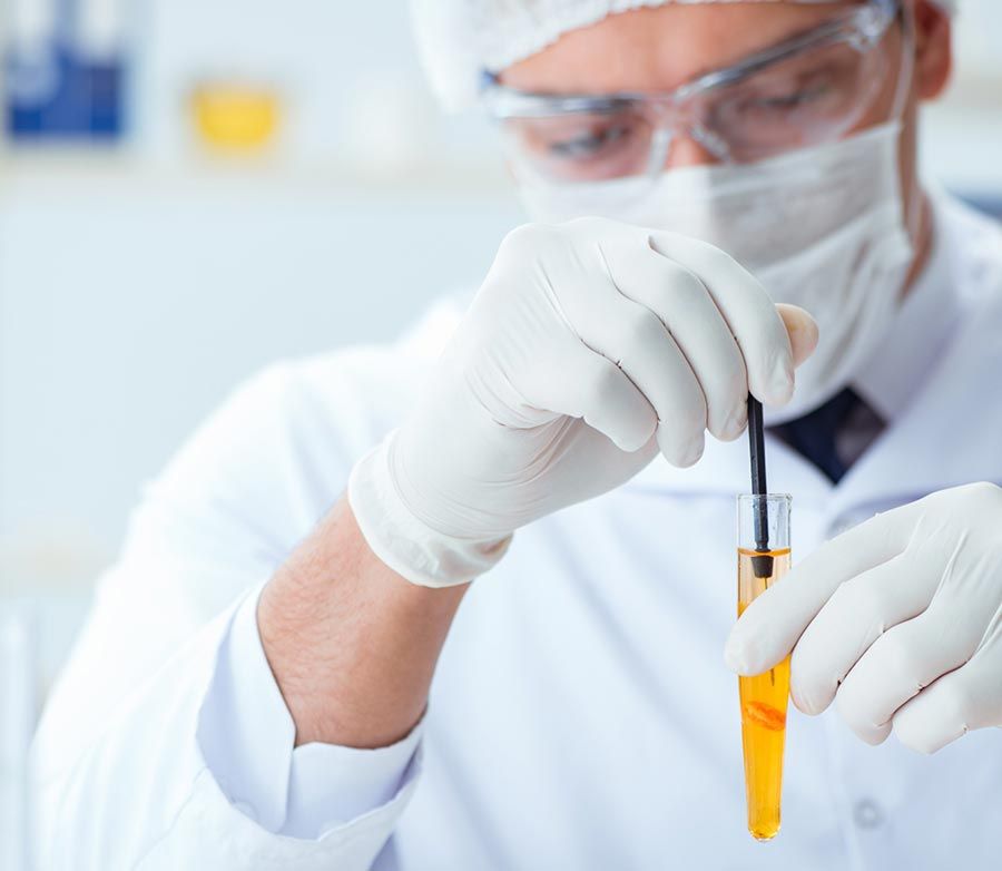 Un hombre que lleva una máscara y guantes sostiene un tubo de ensayo con un líquido amarillo en su interior.