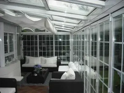 Terraza acristalada con paredes de cristal, molduras blancas y muebles en blanco y negro.