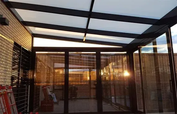 Patio exterior con marco negro, puertas de cristal y techo translúcido. La luz dorada lo atraviesa.
