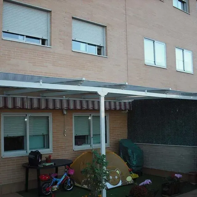 Patio trasero con patio cubierto, bicicleta de niño y una carpa contra un edificio de ladrillos.
