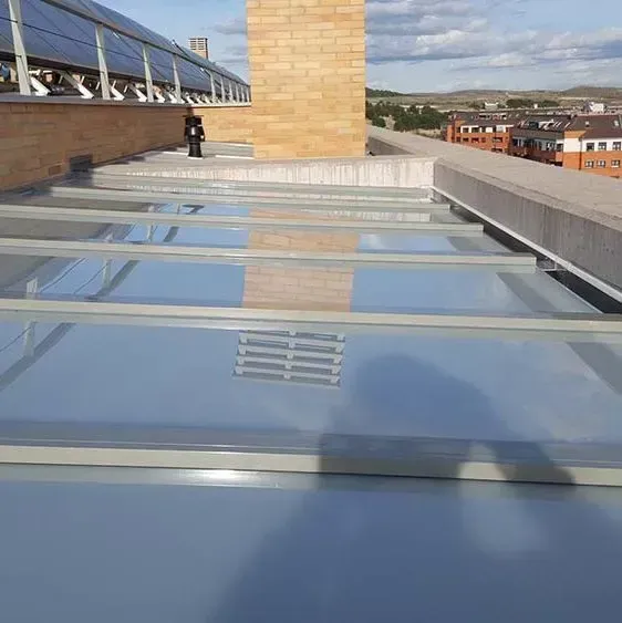 Un tejado plano con paneles de vidrio. Una persona está de pie junto a una chimenea de ladrillo. Se ven paneles solares y edificios.